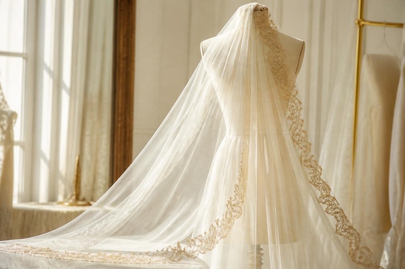 Sheer ivory bridal veil with a gold embroidered scalloped border on a dress form